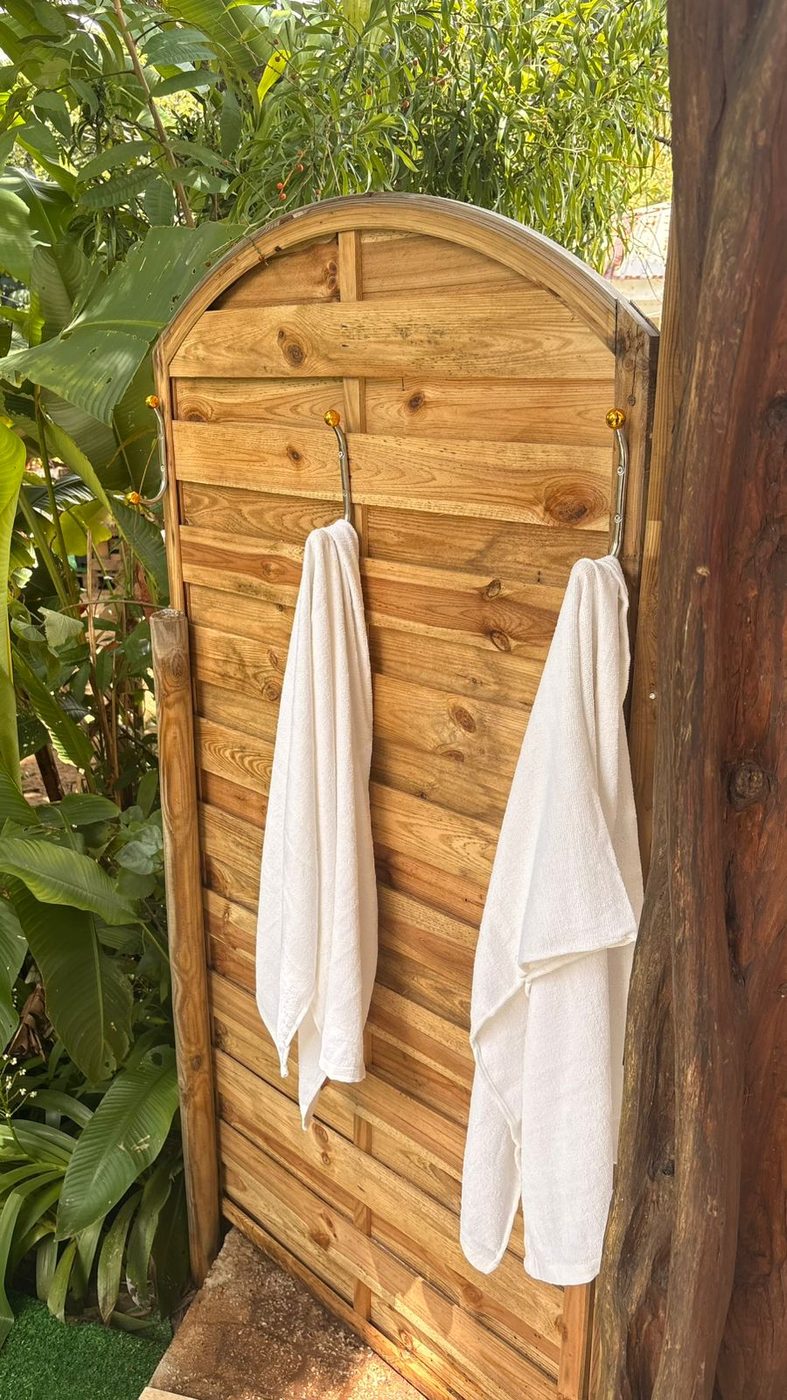 Douche extérieure en bois avec serviettes blanches, ouverte sur la végétation